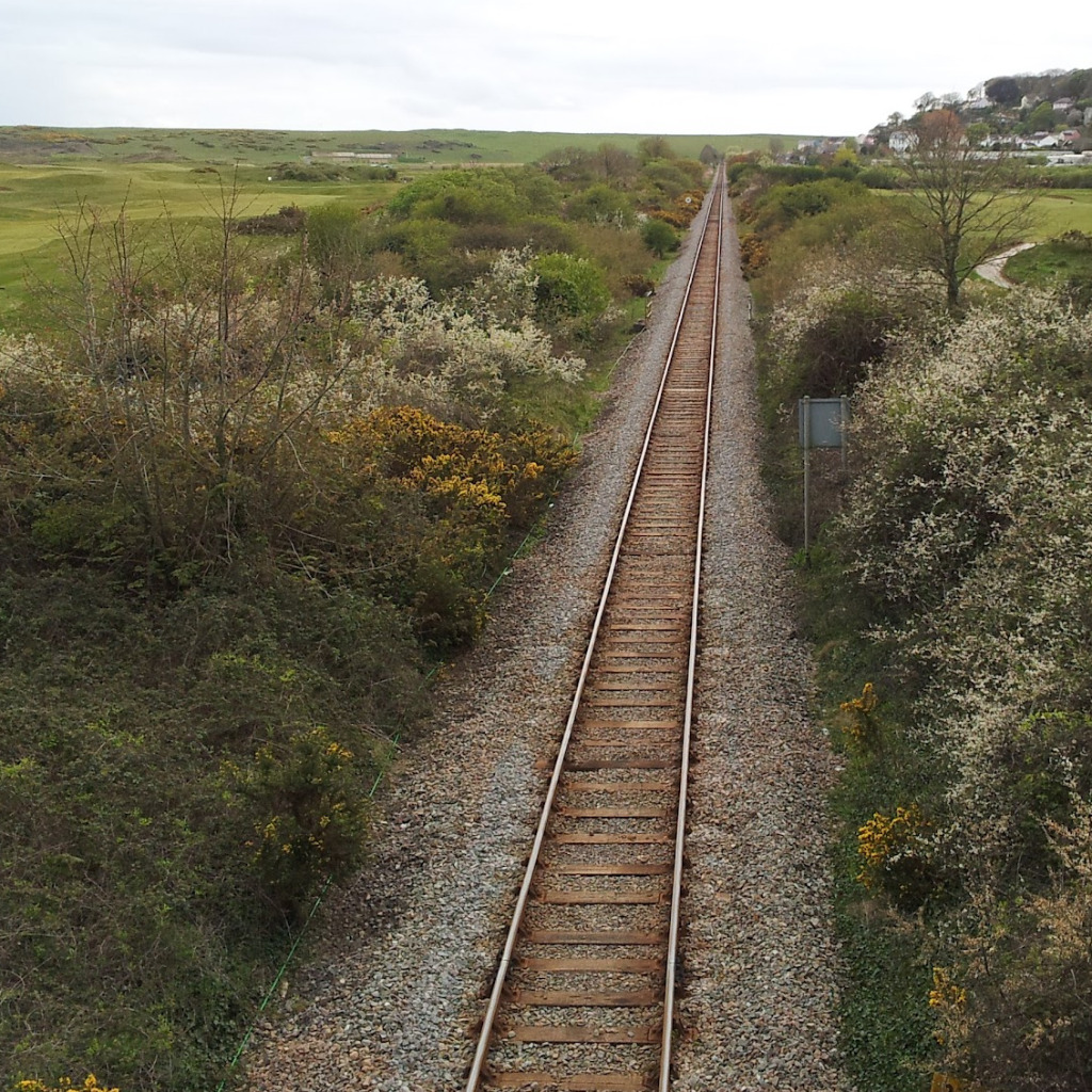 A view looking down from a bridge of a single track railway line disappearing into the distance in a straight line.