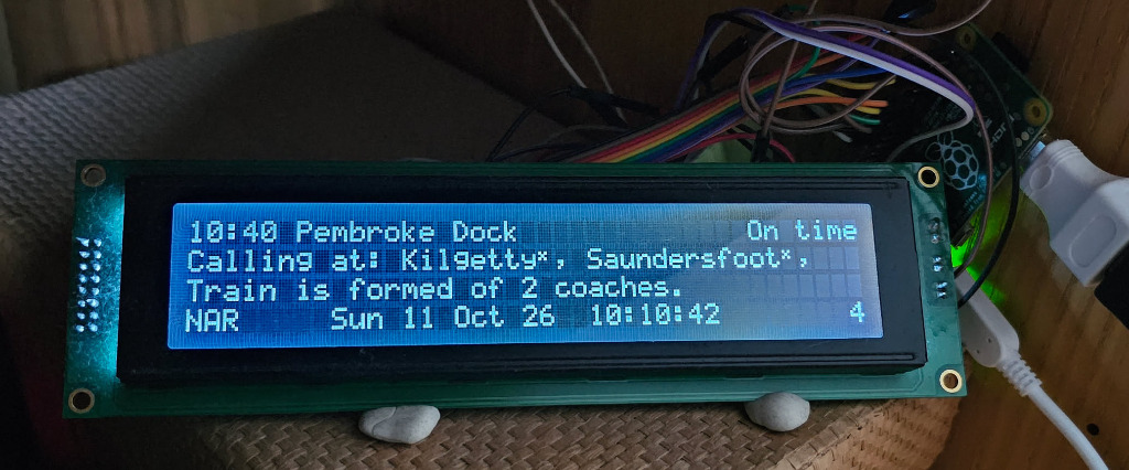 A character LCD display is attached with many, many wires to a Raspberry Pi Zero. It's showing an upcoming train service to Pembroke Dock, currently on time and due at 10:40. Two calling points are shown as Kilgetty and Saundersfoot, as well as a message stating that the train is formed of 2 coaches.