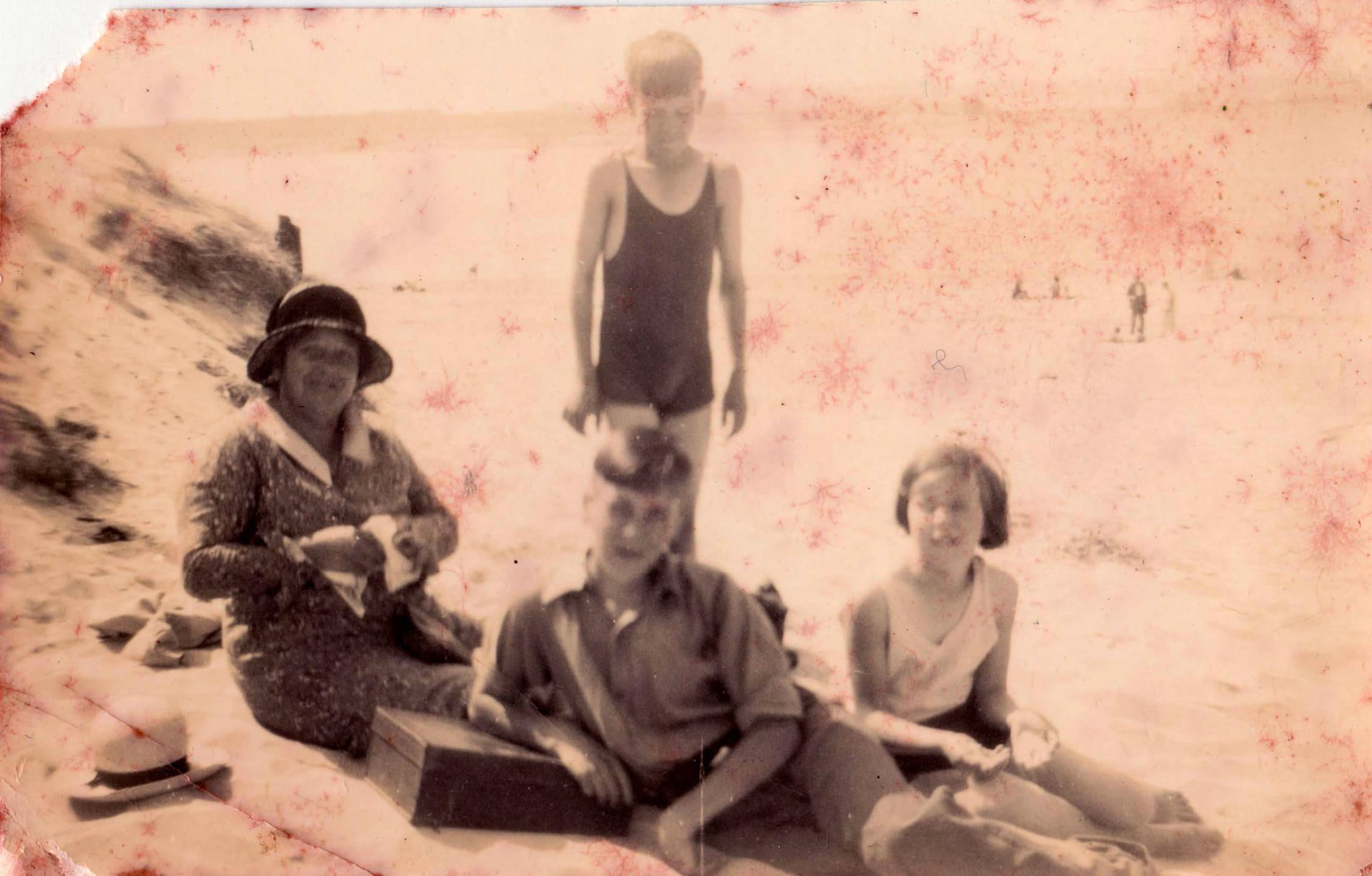 A mother with her 3 children sitting on a sandy beach. The mother is aged in her early 40s, the children aged in their late 10s-early teens.